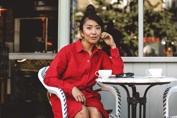 Celeste Wong sitting at a cafe table with a coffee wearing a red outfit.